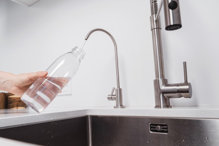 Woman gets filtered water from stainless faucet into reusable bottle