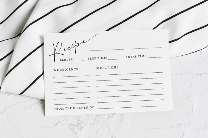 A single blank printable recipe card template featuring a minimalist layout, resting on a black and white striped kitchen towel.