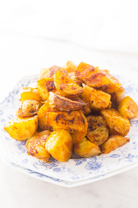 Plated Browned and Crispy Oven Roasted Potatoes Recipe piled on a blue and white stacked decorative serving plate.