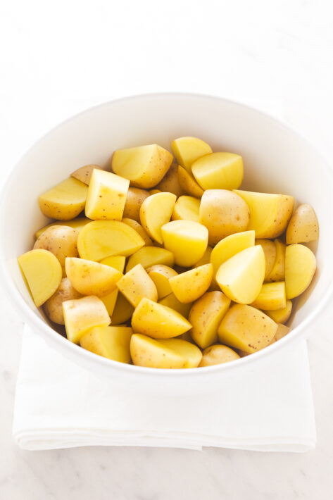 Raw yellow potatoes chopped into bite-sized chunks in a white bowl for a Crispy Oven Roasted Potatoes Recipe.