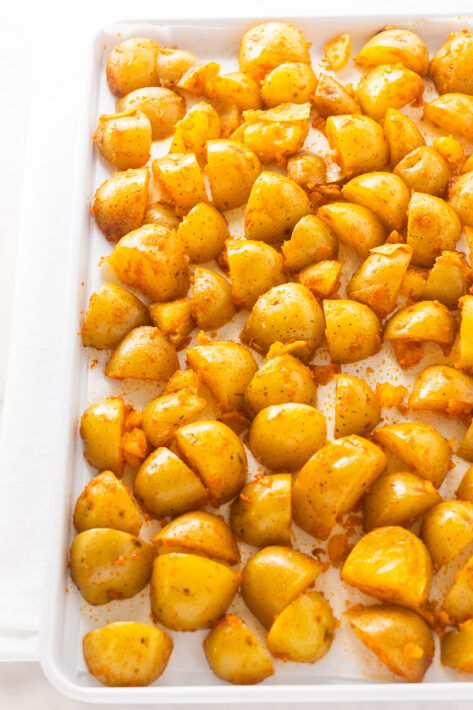 Raw potato chunks tossed in oil and smoked paprika on a parchment-lined baking sheet for a Crispy Oven Roasted Potatoes Recipe.
