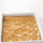 The peanut butter oat flour dough pressed into a square pan to form the base of the no bake peanut butter bars.