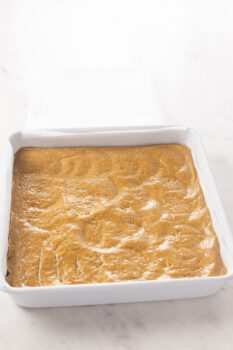 The peanut butter oat flour dough pressed into a square pan to form the base of the no bake peanut butter bars.