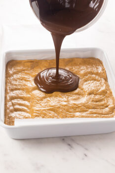 Melted peanut butter chocolate topping being poured over the no bake peanut butter bar base.