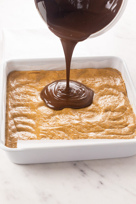 Melted peanut butter chocolate topping being poured over the no bake peanut butter bar base.