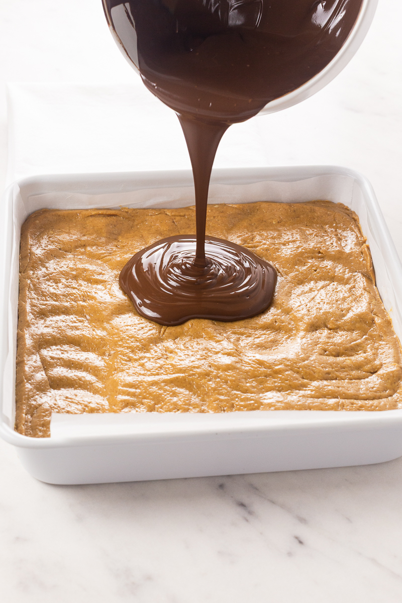 Melted peanut butter chocolate topping being poured over the no bake peanut butter bar base.