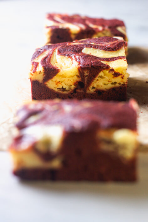 A line of Red Velvet Cheesecake Brownies on a marble surface, emphasizing the consistent marbling and creamy cheesecake swirls across multiple bars.