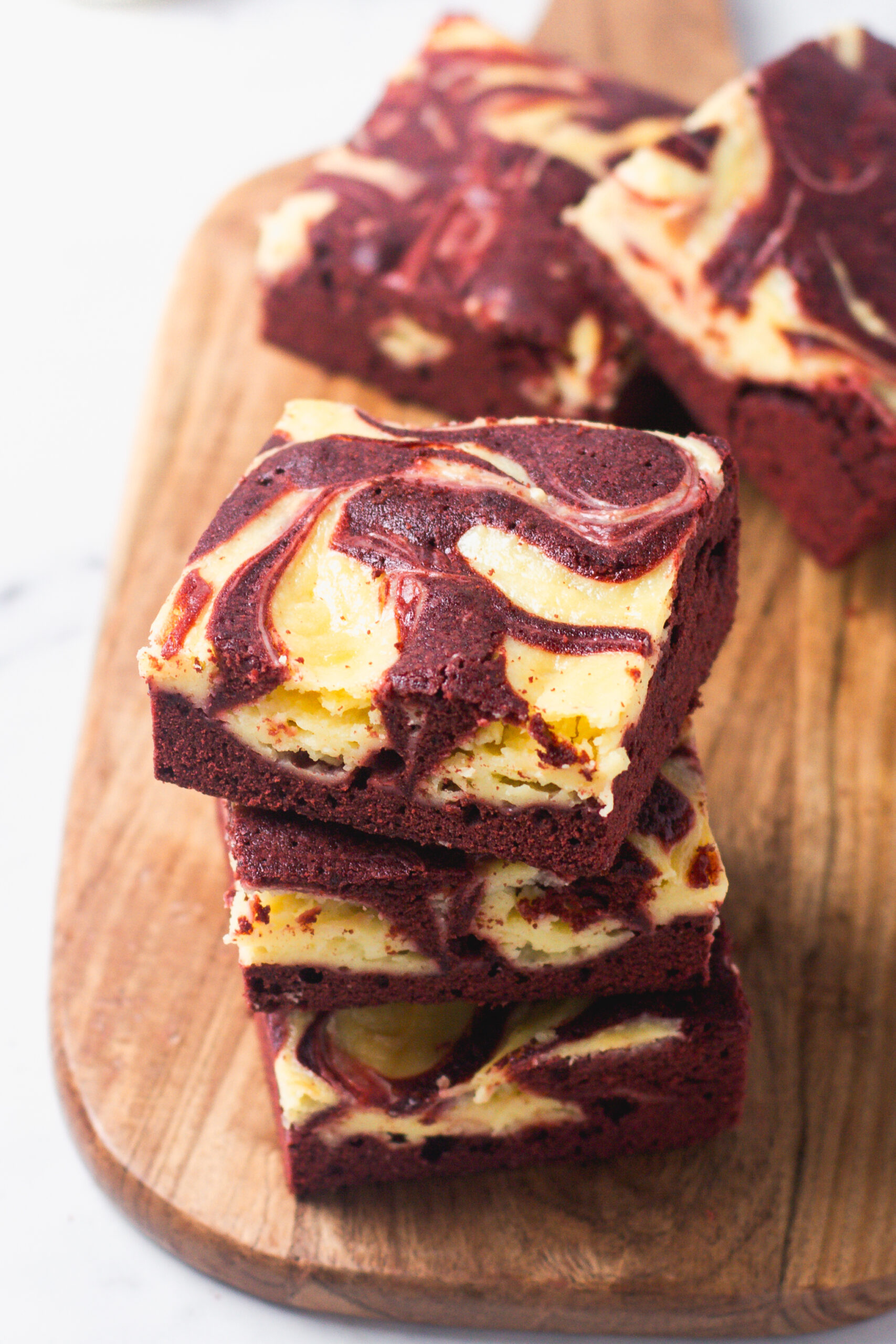 A stack of three Red Velvet Cheesecake Brownies on a wooden serving board showing the fudgy texture and cream cheese swirl.