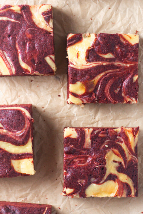Overheard view of four sliced Red Velvet Cheesecake Brownies on parchment paper highlighting the marbled red and white pattern.