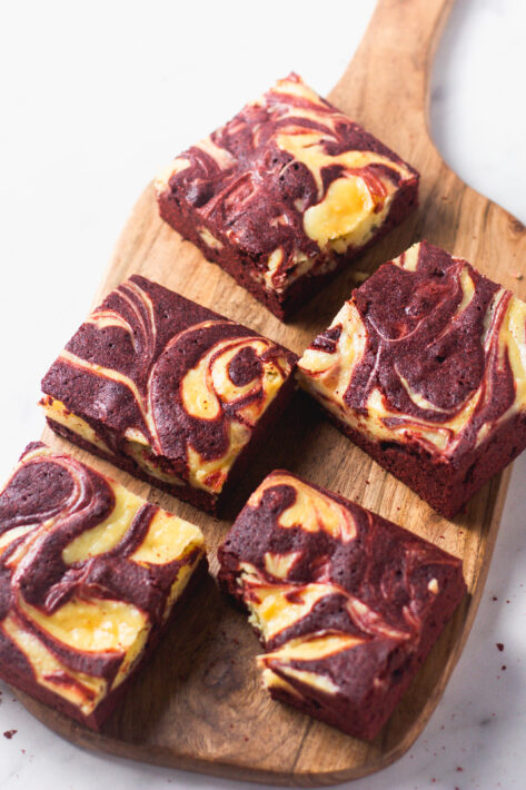 A wooden platter of sliced Red Velvet Cheesecake Brownies ready to serve, showing the contrast between the crimson base and white swirl.A wooden platter of sliced Red Velvet Cheesecake Brownies ready to serve, showing the contrast between the crimson base and white swirl.